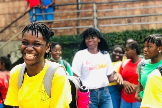 a girl wearing a backpack, standing with her peers, smiles at the camera